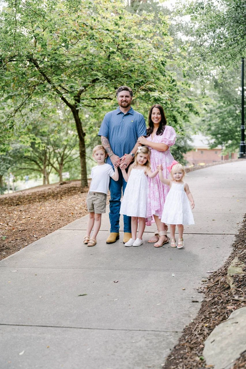 Two adults and three children standing together on a tree-lined path